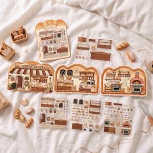 Op de afbeelding: Een verzameling stickervellen met een bakkerijthema en kleine broodvormige bedels. De stickers bevatten illustraties van winkelpuien, ovens, planken en diverse bakproducten. De bedels zijn beige en bruin en hebben de vorm van kleine broodjes.