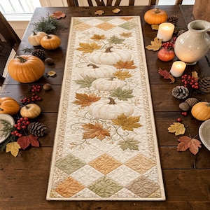 May include: A rectangular quilted table runner featuring a central design of white pumpkins and autumn leaves in shades of orange, yellow, and green. The ends of the runner are decorated with a diamond pattern in muted earth tones and cream.