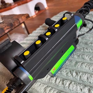 Könnte beinhalten: Ein schwarzes Metall-Detektor-Steuergehäuse mit fünf gelben runden Drehknöpfen, einem schwarzen Schutzrahmen und einem grün-blauen Etikett mit dem weißen Aufdruck EXCALIBUR II und Waterproof NiMH Rechargeable Battery Pack.