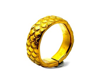 Op de afbeelding: Een gouden ring met een getextureerd oppervlak met een herhalend patroon van overlappende schubben. De band heeft een afgeronde buitenkant en een gladde binnenkant, met een zichtbaar scharniermechanisme aan de basis van de ring.