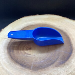 May include: A blue plastic scoop with a handle. The scoop is on a wooden surface.