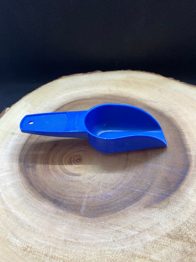 May include: A blue plastic scoop with a handle. The scoop is on a wooden surface.