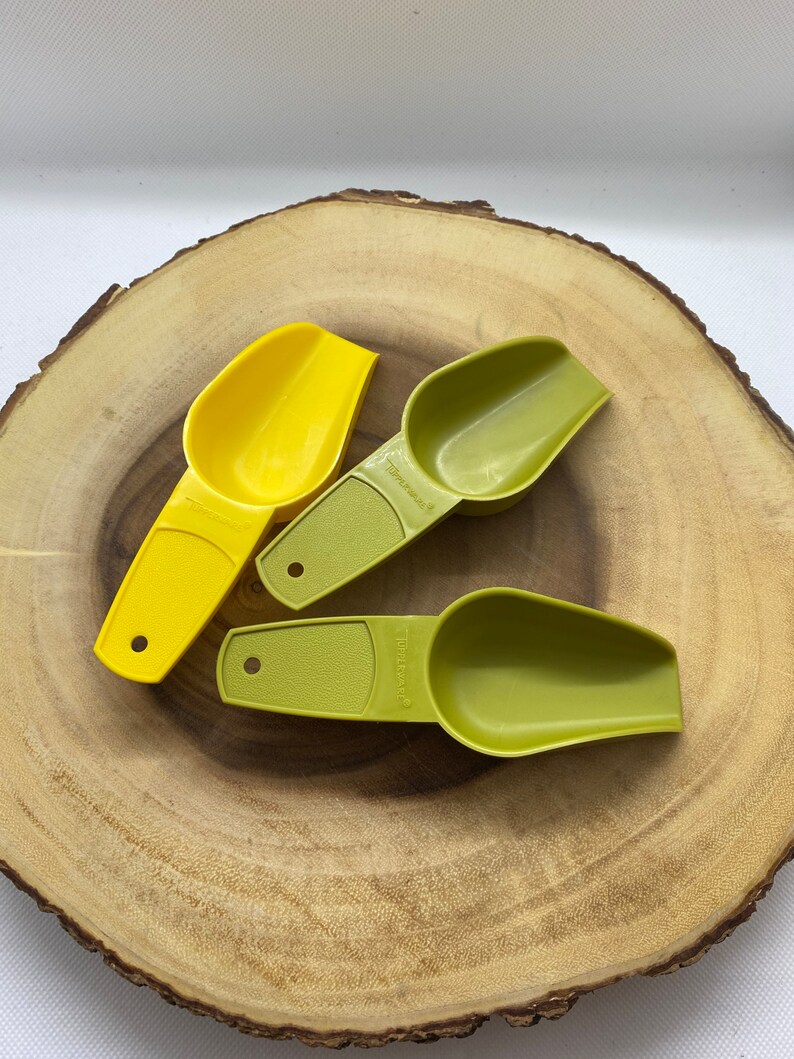 May include: Three plastic measuring scoops, two green and one yellow, on a wooden surface. The scoops are labeled "Tablespoon" and "Teaspoon".