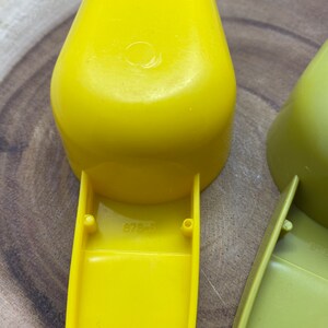May include: Two yellow plastic measuring scoops with a handle. The larger scoop has the number "878-5" printed on the bottom.