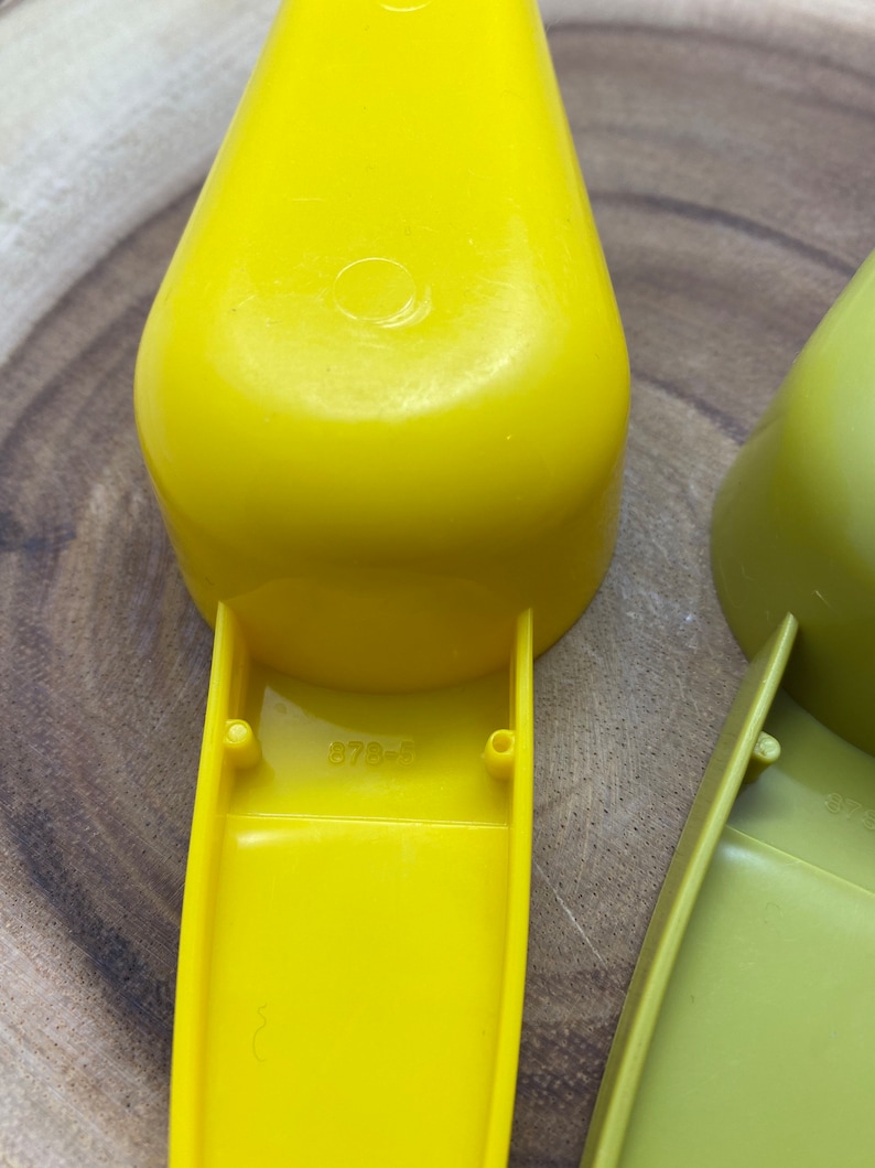 May include: Two yellow plastic measuring scoops with a handle. The larger scoop has the number "878-5" printed on the bottom.