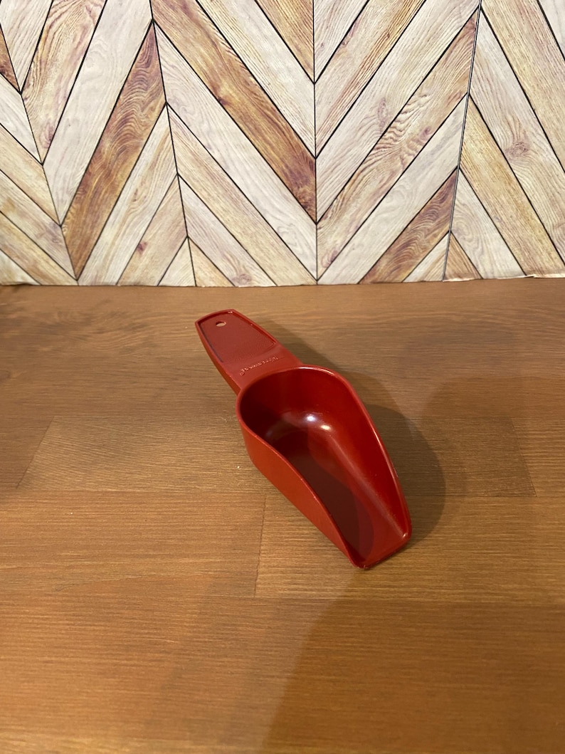 May include: A red plastic scoop with a handle. The scoop is designed for measuring dry ingredients.