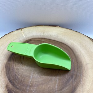 May include: A green plastic scoop with a handle. The scoop is on a wooden surface.