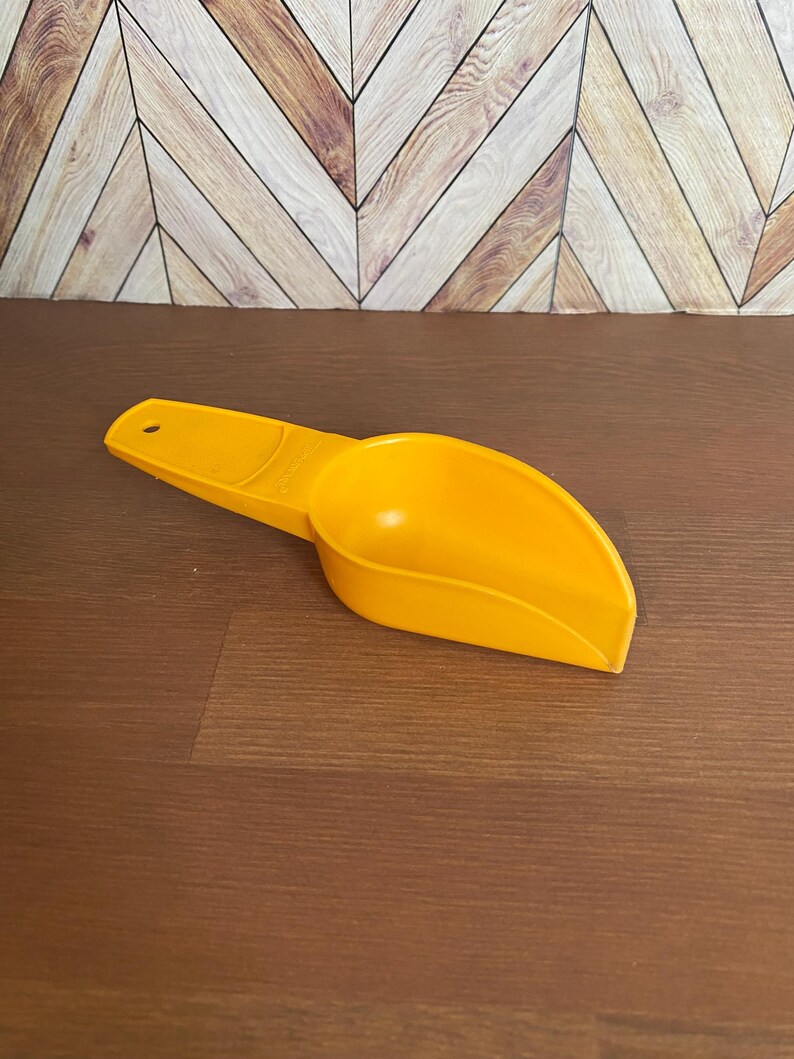 May include: A yellow plastic scoop with a handle. The scoop is designed for measuring dry ingredients.