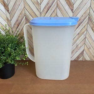 May include: A clear plastic pitcher with a light blue lid. The pitcher has a handle and is sitting on a wooden surface.