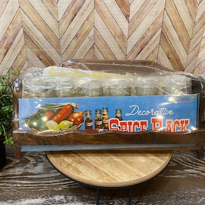 May include: A wooden spice rack with a blue and white label that reads "Decorative Spice Pack". The rack is filled with clear glass jars and is wrapped in plastic.
