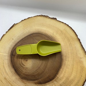 May include: A green plastic scoop with a handle. The scoop is on a wooden surface.