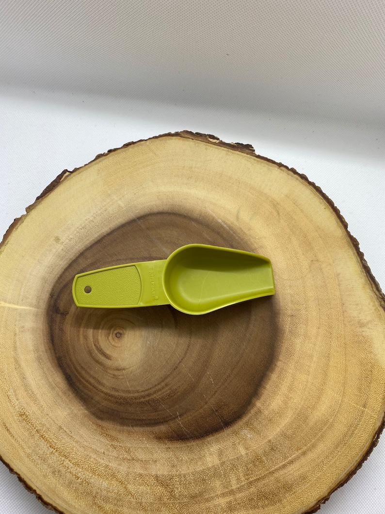 May include: A green plastic scoop with a handle. The scoop is on a wooden surface.