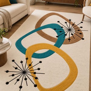 May include: A rectangular area rug with a cream-coloured base featuring three large, overlapping rounded geometric shapes in brown, teal, and mustard yellow. The design includes two black starburst patterns with thin lines and circular dots.
