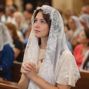 May include: A white lace chapel veil featuring a delicate floral pattern with scalloped edges. The veil is draped over the head, covering the hair and shoulders, and is crafted from a fine, semi-sheer fabric with intricate embroidery details.