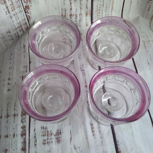 May include: A set of four clear glass bowls, each featuring a distinct pink rim and a textured pattern along the interior walls. The bowls have a circular base and a wide opening, showcasing a consistent design across all four individual pieces.