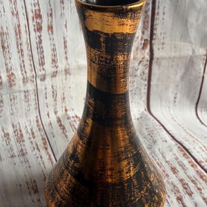 May include: A vase with a flared neck and a wide, rounded base. The exterior features a textured, distressed finish with alternating horizontal bands of metallic copper and matte black, while the interior rim is finished in a solid black.