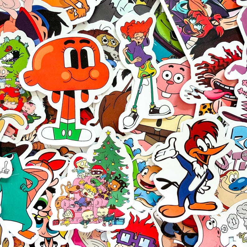 May include: A collection of assorted vinyl stickers featuring various cartoon characters, including a bright orange fish, a red-headed person in a purple shirt, and a woodpecker, alongside a festive scene with characters gathered around a tree.