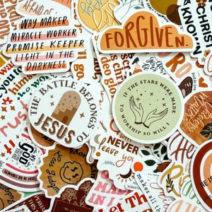 May include: A collection of assorted vinyl stickers featuring various religious and inspirational phrases in earthy tones. Visible text includes Way Maker, Miracle Worker, Promise Keeper, Light in the Darkness, Forgiven, The Battle Belongs to Jesus, and If the Stars Were Made to Worship So Will I.