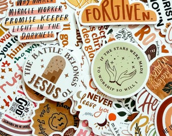 May include: A collection of assorted vinyl stickers featuring various religious and inspirational phrases in earthy tones. Visible text includes Way Maker, Miracle Worker, Promise Keeper, Light in the Darkness, Forgiven, The Battle Belongs to Jesus, and If the Stars Were Made to Worship So Will I.