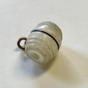May include: A clear, cylindrical bottle stopper with a black band and a small, gold-colored ring. The stopper has a textured, layered appearance. The object is likely made of glass or a similar material.