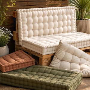 May include: A wooden pallet sofa base featuring a large cream-colored tufted cushion set. Additional floor cushions in solid terracotta, olive green, and cream are arranged nearby. The pallet is marked with an EPAL stamp on the side frame.