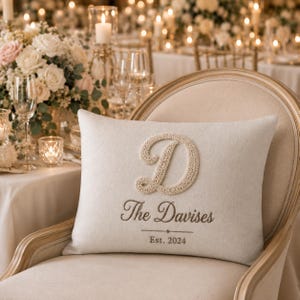 Peut inclure: Un coussin rectangulaire blanc cassé orné d'une grande lettre D brodée en relief de couleur crème. Sous la lettre, le texte indique The Davises, suivi d'une ligne horizontale et de l'inscription Est. 2024 en fil marron foncé.
