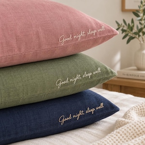 May include: A stack of three rectangular pillows in dusty pink, sage green, and navy blue. Each pillow features a textured fabric finish and the embroidered white cursive text "Good night, sleep well" positioned on the lower right side.