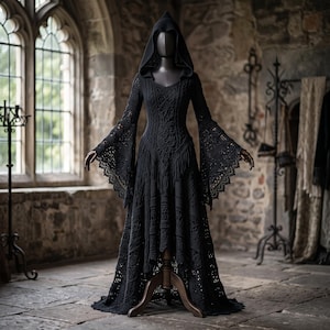 May include: A floor-length black dress featuring an intricate crochet pattern, a pointed hood, and long flared sleeves with scalloped edges. The garment has a fitted bodice with a textured design and a flowing skirt that reaches the floor.