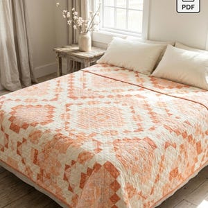 May include: A bed quilt featuring a geometric patchwork pattern in shades of peach, coral, and cream. The design consists of repeating square and diamond motifs across the fabric surface, covering a bed with two cream-colored pillows.