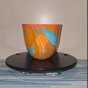May include: A bowl with a marbled pattern featuring vibrant swirls of bright orange, light blue, and yellow. The bowl has a smooth, rounded exterior and a wide, open top, showcasing a fluid, multi-coloured design across its entire surface.