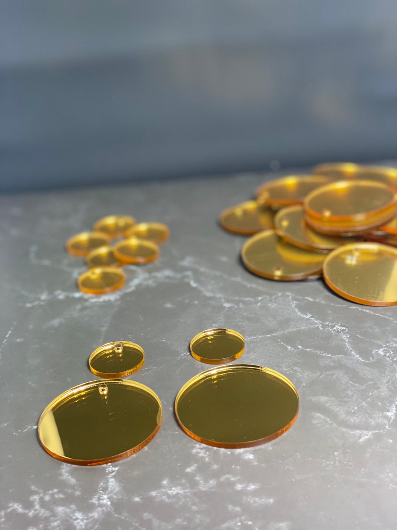 May include: A selection of gold-coloured, oval-shaped acrylic blanks. The blanks are of varying sizes, some with a small hole at the top for hanging. The reflective surface of the blanks creates a mirror-like effect. Suitable for craft projects.