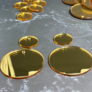 May include: Various gold-coloured acrylic blanks in oval and circular shapes, ideal for crafting. The blanks have small holes and come in different sizes, with larger ovals and smaller circles. The reflective surface gives them a shiny appearance.