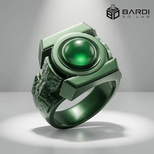 Può includere: Un anello verde scuro con una gemma circolare verde centrale incastonata in una cornice geometrica. La fascia presenta una finitura ruvida e rocciosa sui lati. Il logo BARDI 3D LAB è visibile nell'angolo in alto a destra dell'immagine.