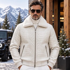 May include: A white bomber jacket featuring a textured crocodile skin pattern, a thick white faux fur collar, a central silver zipper, and two zippered side pockets. The jacket has ribbed cuffs and a ribbed hem, worn over a white turtleneck sweater.