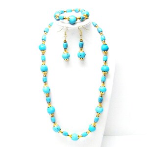 May include: A jewelry set consisting of a necklace, a bracelet, and a pair of drop earrings. Each piece features round and cylindrical turquoise-colored beads with black veining, accented by small gold-toned metal caps and spacers throughout.