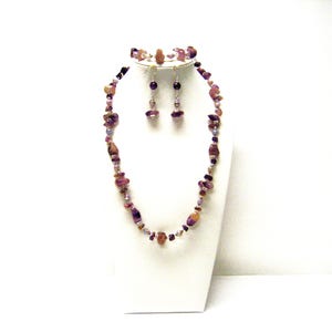 以下が含まれることがあります： 紫と茶色の宝石のネックレス、ブレスレット、イヤリングのセット。ジュエリーは、小さく不規則な形の石で作られています。