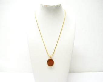 May include: A gold-toned chain necklace featuring a single, smooth, teardrop-shaped pendant in a warm, translucent amber color. The pendant is encased in a thin gold-toned metal frame, suspended from a simple, slender gold-toned chain.