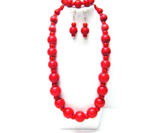 May include: A red beaded jewelry set including a necklace, bracelet, and earrings. The necklace and bracelet feature large, round beads. The earrings have two smaller beads. The jewelry is displayed on a white surface.