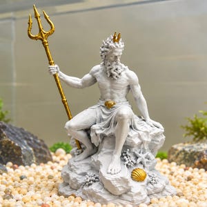 Könnte beinhalten: Eine steingraue Figur eines bärtigen Wesens, das auf einem Felsen sitzt und einen hohen goldenen Dreizack hält. Die Figur trägt eine goldene Krone und eine goldene Gürtelschnalle. Der Sockel ist mit modellierten Muscheln und Korallen verziert.