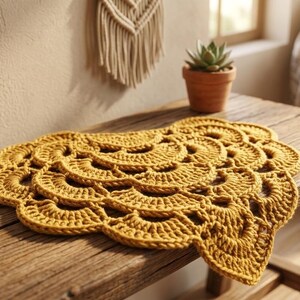 Puede incluir: Un tapete de ganchillo color amarillo mostaza con un patrón repetitivo en forma de abanico y bordes festoneados. La pieza textil circular está elaborada con hilo grueso, mostrando un diseño texturizado y superpuesto que irradia desde el centro hacia afuera.