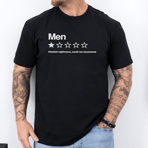 Peut inclure: Un t-shirt noir à manches courtes avec le texte blanc Men au-dessus d'une étoile pleine et de quatre contours d'étoiles vides. Sous les étoiles, le texte indique Absolute nightmares, would not recommend. Le t-shirt a un col rond.