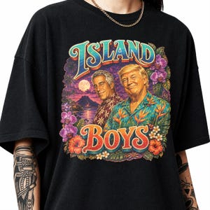 Pode incluir: Uma t-shirt preta de manga curta com uma estampa gráfica colorida de dois homens em camisas tropicais. O design inclui o texto ISLAND BOYS, uma paisagem de pôr do sol com um vulcão e flores de hibisco roxas e laranjas.