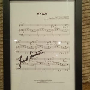 May include: A framed musical score for the song My Way, featuring printed lyrics and notes on white paper. The sheet music includes the title My Way, credits for Paul Anka, and a prominent black ink signature of Frank Sinatra across the staff lines.