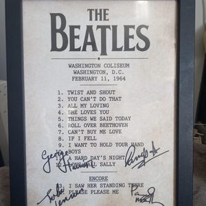 May include: A framed print featuring The Beatles concert setlist from the Washington Coliseum on February 11, 1964. The off-white paper displays the band name, venue details, a numbered list of twelve songs, an encore section, and four signatures.
