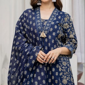 May include: A dark blue long-sleeved tunic featuring a repeating gold floral pattern, a V-neckline with a decorative border, and a central beige tassel detail. The garment includes a matching draped fabric piece worn over the shoulder.