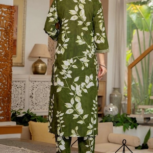 Pu&ograve; includere: Una tunica verde oliva a maniche lunghe con un motivo a foglie bianche e un colletto alto con bordo decorativo, abbinata a pantaloni dritti coordinati che presentano la stessa stampa a foglie bianche su tutto il tessuto.