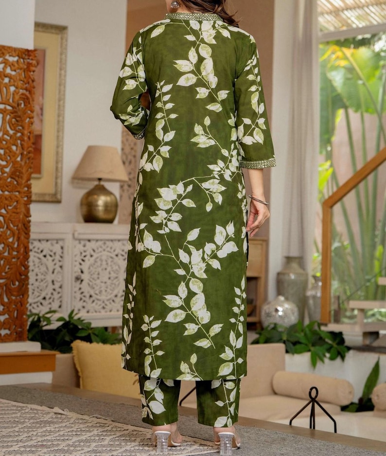 Pu&ograve; includere: Una tunica verde oliva a maniche lunghe con un motivo a foglie bianche e un colletto alto con bordo decorativo, abbinata a pantaloni dritti coordinati che presentano la stessa stampa a foglie bianche su tutto il tessuto.