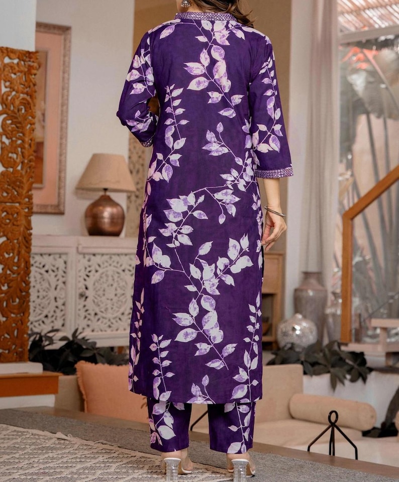 Pu&ograve; includere: Un completo composto da una tunica a maniche lunghe e pantaloni abbinati di colore viola scuro con un motivo a foglie e viticci bianchi. La tunica presenta uno scollo alto con bordo decorativo e maniche a tre quarti con polsini rifiniti.