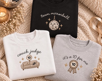 May include: Three crewneck sweatshirts in black, white, and grey. The black sweatshirt features an embroidered disco ball and the text "team mirrorball". The white sweatshirt shows a couch with a "10" sign and "couch judge". The grey one has a "10" ribbon and "it's a 10 for me".