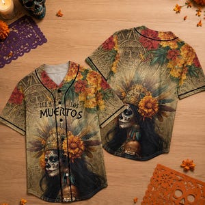 May include: A button-down baseball jersey featuring a graphic print of a person with sugar skull makeup, adorned with marigold flowers and an ornate headdress. The text "LOS MUERTOS" is printed on the front. The design includes a tan background.